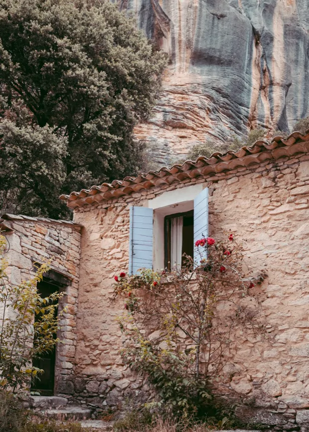 A stone house with a blue shutter, beneath the valley's rock face
